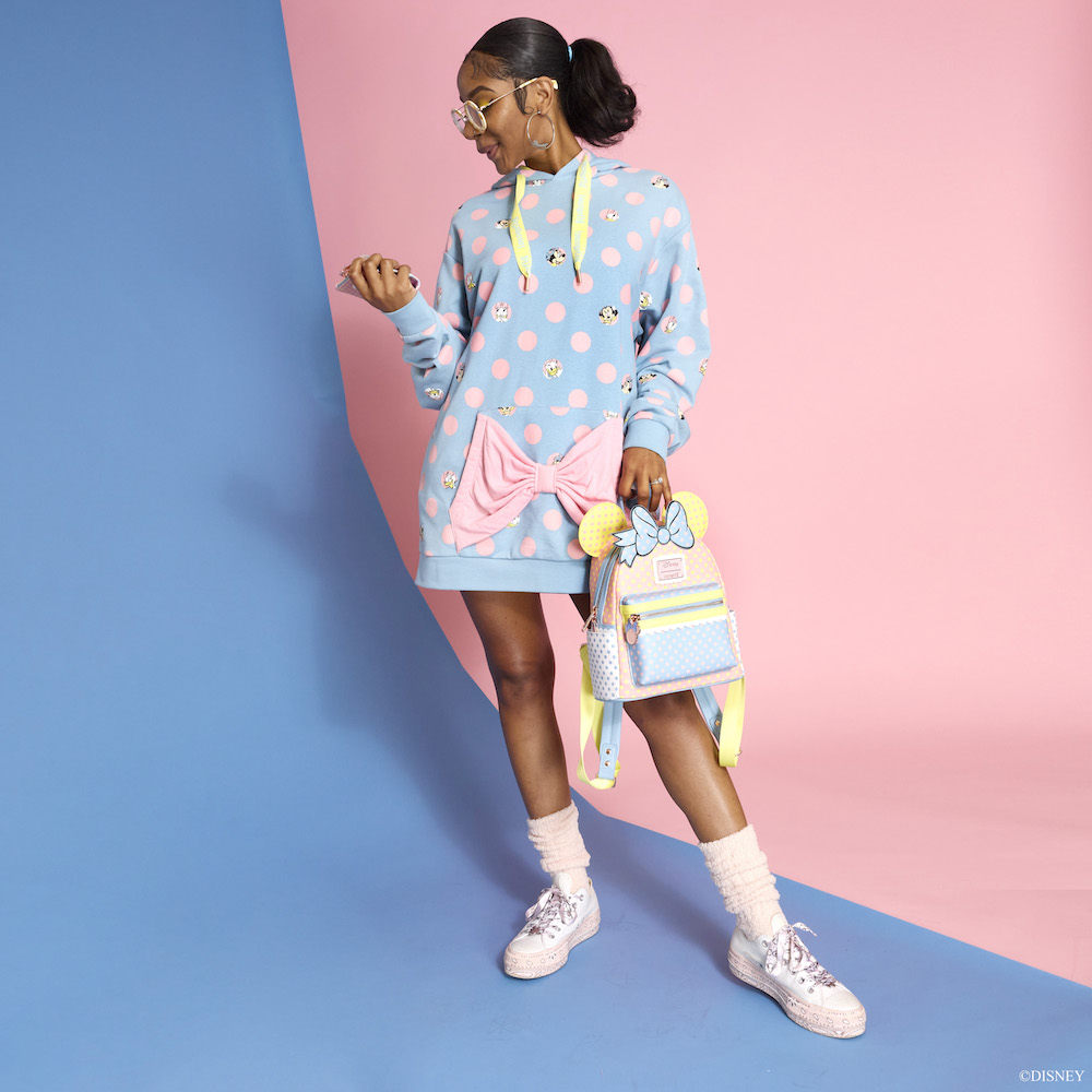 Woman modeling the Minnie Mouse Pastel Polka Dot Unisex Hoodie and Mini Backpack against a pastel color block background